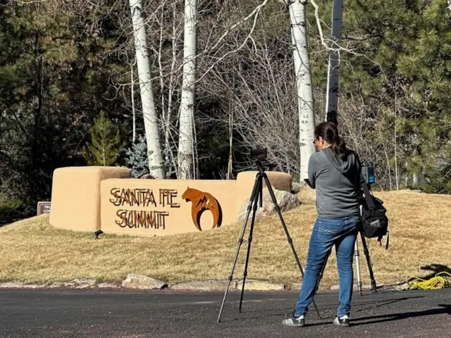 Mulher com câmera no tripé em frente a entrada de condomínio