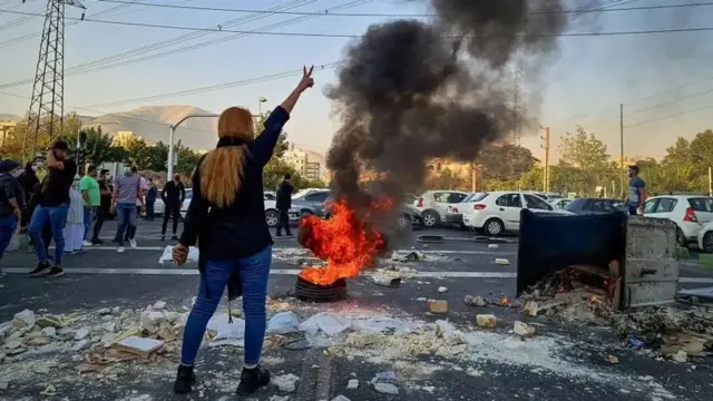 یک تجمع و زنی که دستش را به علامت پیروزی بالا برده. یک لاستیک خودرو در حال سوختن