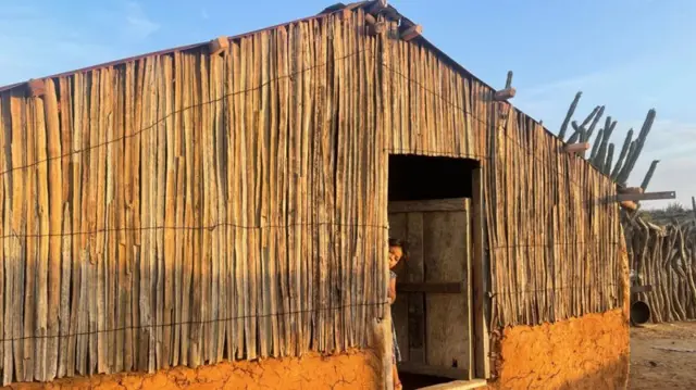 Mulher olha pela porta de uma casa tradicional de barro e cacto no norte da Colômbia