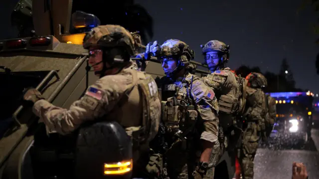 Uzbrojeni i zamaskowani agenci FBI stojący nocą obok opancerzonego pojazdu.