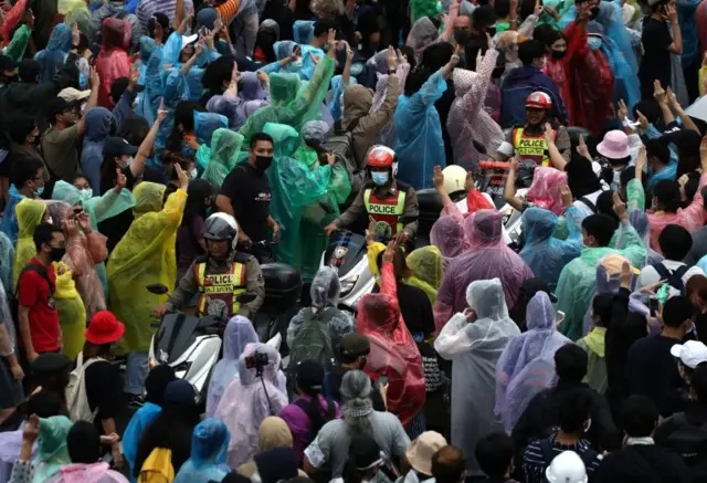 Pro-democracy protesters show the three-finger salute as police officers drive by during an anti-government protest, in Bangkok, Thailand October 17, 2020