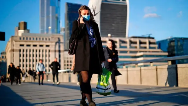 A woman wearing a protective face mask speaks on the phone as she crosses London Bridge