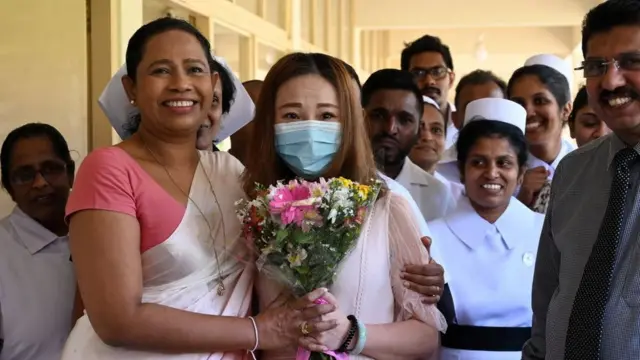 A Chinese tourist (C), who was tested positive for the COVID-19 coronavirus and isolated for treatment, poses for photographs with Sri Lankan Health Minister Pavithra Wanniarachchi (front L) and medical staff after she was discharged from the main infectious diseases hospital near Colombo on February 19, 2020, following her recovery. - The 43-year-old woman, the first and only COVID-19 patient in Sri Lanka, was admitted to the hospital on January 25 and tested positive for COVID-19 two days later.
