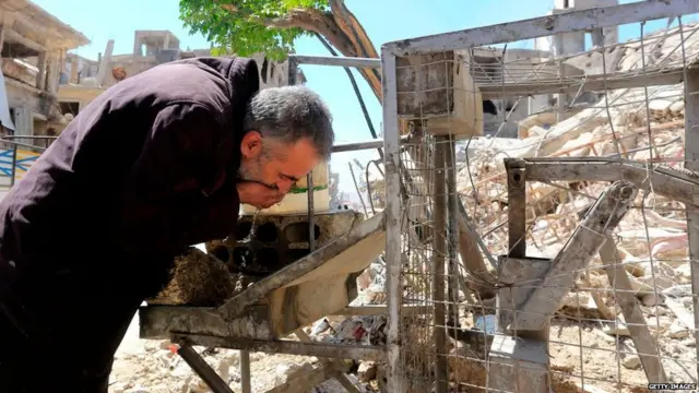 Syrian man drinks water in a destroyed street in Douma on the outskirts of Damascus on April 16, 2018