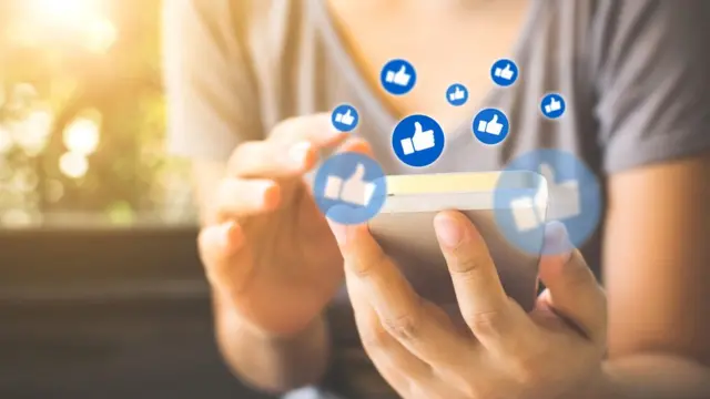 Mujer con un celular y los signos de me gusta de Facebook.