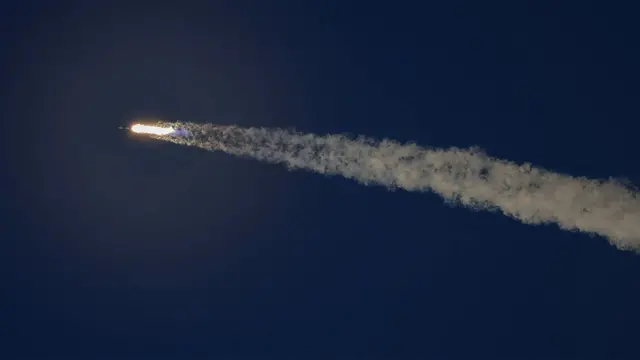 一枚火箭拖着长长的白色尾焰，在深蓝色天空中高速升空。画面聚焦于火箭及其尾迹，背景没有其他物体。