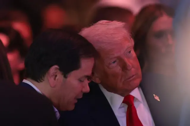 観客に囲まれたトランプ氏の耳元で話すルビオ氏