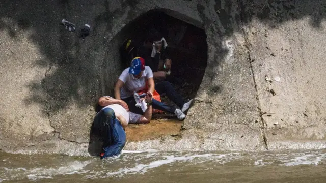 Un manifestante que cruzó el Guaire recibe asistencia al desplomarse frente a un desagüe que da al río.