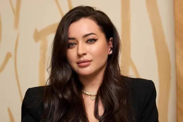 Олександра Постоловська, жінка-брюнетка в чорному костюмі на теплому золотавому фоні