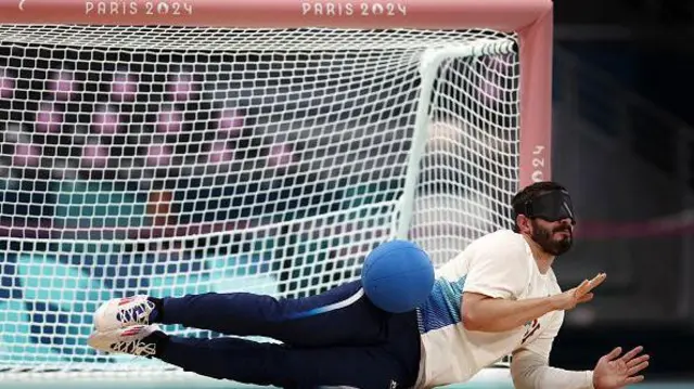Un athlète paralympique aux yeux bandés joue au Goalball sur le sol.