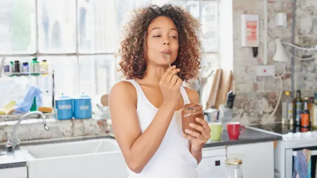 Imagem mostra mulher magra comendo docecáixa loteriasuma cozinha