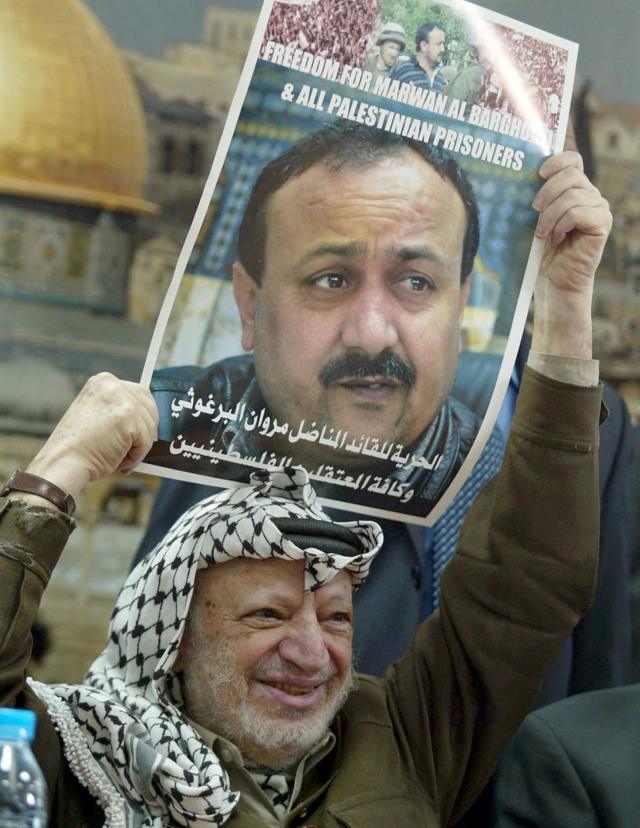 Palestinian leader Yasser Arafat holds a poster of jailed leader of the Fatah movement in the West Bank and leading proponent of the Palestinian uprising Marwan Barghouti during a ceremony in in the West Bank city of Ramallah on 12 February 2004