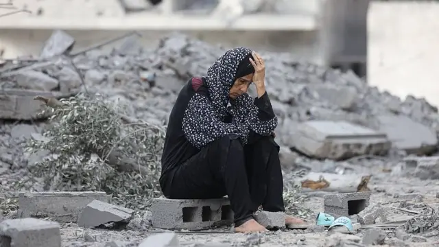 Mujer desolada sentada entre escombros sosteniéndose la cabeza 