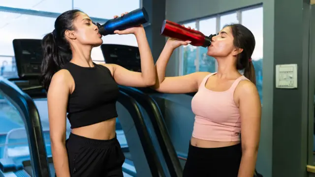 महिला जिम में खड़ी होकर पी रही है