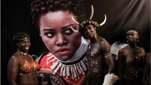Wacheza sarakasi wakisimama karibu na picha ya Lupita Nyong'o katika uzinduzi wa Black Panther Kisumu, Kenya