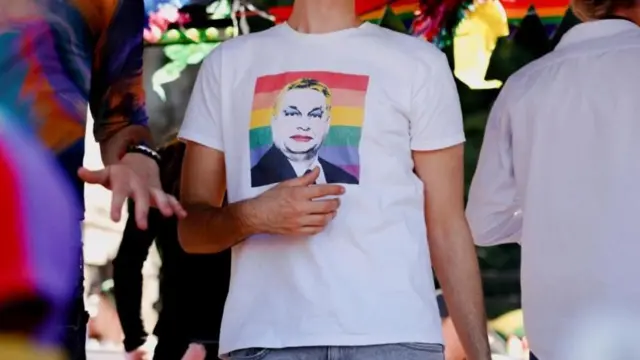 bir kişinin üstünde orban'ın dijital bir şekilde fotoğrafına makyaj eklenmiş fotoğrafının basılı olduğu tişört görülüyor