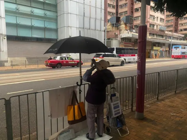 A woman is seen from behind demonstrating in front of a large office building