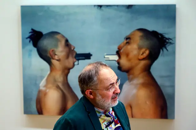 Мужчина в очках и с седой бородкой на фоне картины