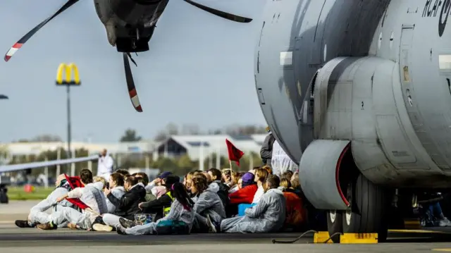 পরিবেশবাদীরা বিমানের চাকার সামনে বসে উড়ান বন্ধ করার চেষ্টা চালায়।