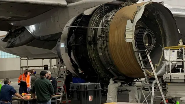 Workers look at the damaged engine on the plane at Denver airport on 22 February 2021
