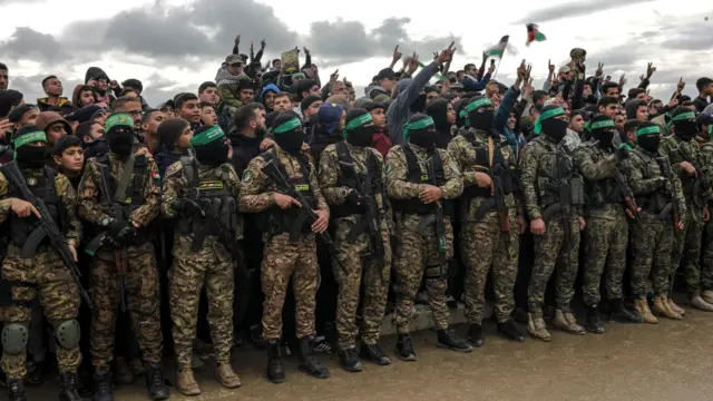 Red naoružanih boraca Hamasa stoji leđima okrenut prema gomili ljudi u civilnoj odeći.