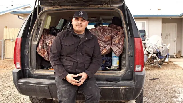 Brandon Billie poses with the car he lives in now