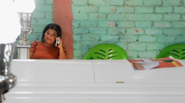 Una mujer habla por celular junto a un ataúd blanco con los restos de una de las personas asesinadas en una mina de Pataz. 