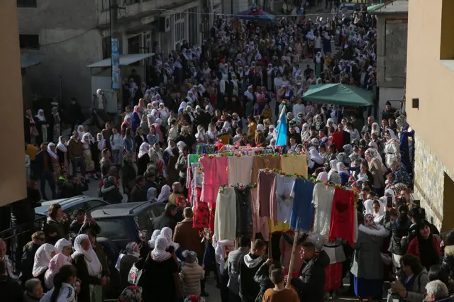 Kolona polako pristiže na trg u centru sela na kojem su već prisutne stotine ljudi.