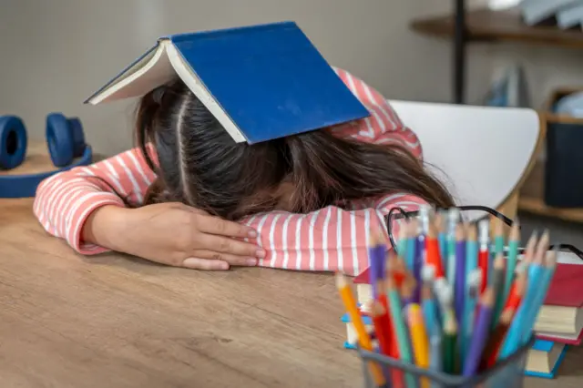 Menina debruçada sobre a mesa com livro em cima da cabeça