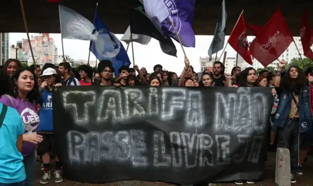 Manifestação contra o aumento das tarifas do transporte sobre trilhos, na Avenida Paulista, em São Paulo, em 4 de janeiro de 2024. Os manifestantes, em sua maioria jovens, carregam bandeiras ligadas a grupos de esquerda e uma grande faixa preta onde se lê "Tarifa não, passe livre já"