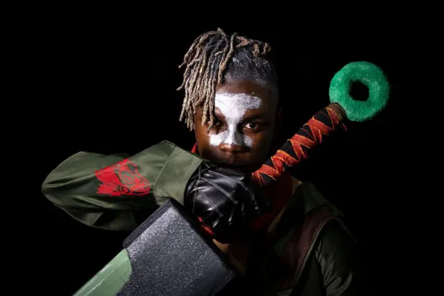 A man poses for the camera wearing white face paint and a toy sword.