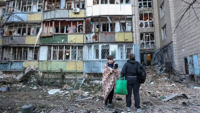 напад на кијев, људи стоје испред једне од погођених зграда у Кијеву