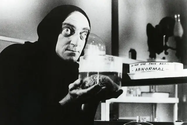 Acteur aux yeux qui sortent de l'orbite et tenant une cervelle entre ses mains.