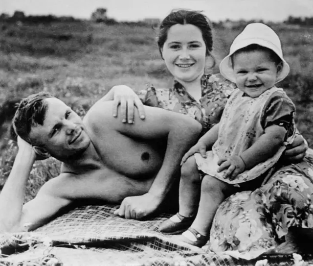 Yuri gagarin yere uzanmış bir şekilde, üstü çıplak, eşi ve yaklaşık 1 yaşında olan kızı da ona yaslanmış şekilde oturuyor.