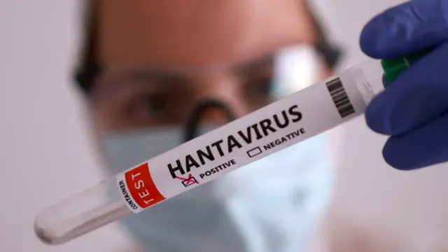 Una persona con mascarilla sostiene un tubo de ensayo etiquetado como "Hantavirus positivo".
