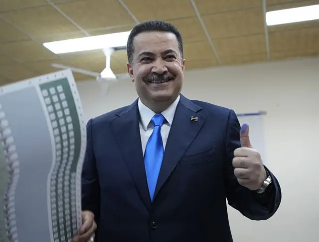 Başbakan Muhammed Şia El Sudani oy kullanırken mürekkeplenmiş parmağını gösteriyor, elinde oy pusulası var ve gülümsüyor 