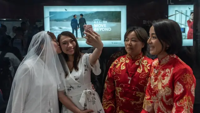 香港某港鐵車站內兩對女同性戀伴侶以站台上一幅由男同性戀伴侶出演的國泰航空公司廣告為背景拍照(25/5/2019)