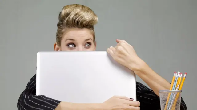 Mujer escondida tras la pantalla de la computadora