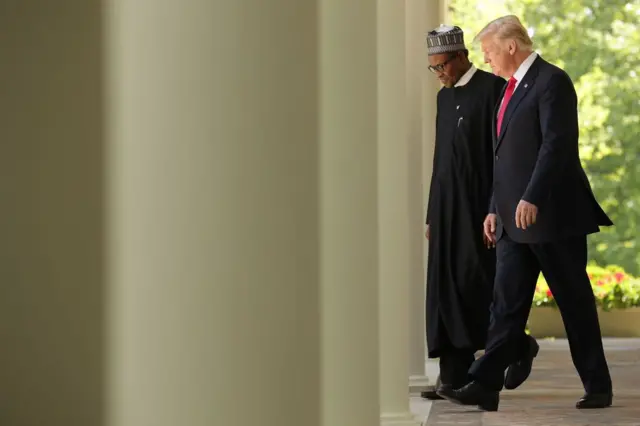 Donald Trump et Muhammadu Buhari - tous deux en tenue de soirée - discutent en passant devant des colonnes à la Maison Blanche.