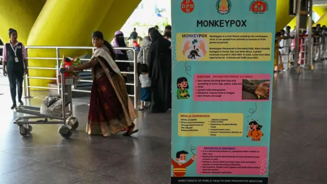 Awọn ero n kọja lẹgbẹ iwe bana to n ṣafihan ilanilọye nipa arun mpox ni papakọ ofurufu Chennai.