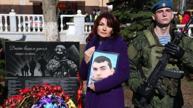 سيدة تحمل صورة شاب وتقف إلى جانب جندي
