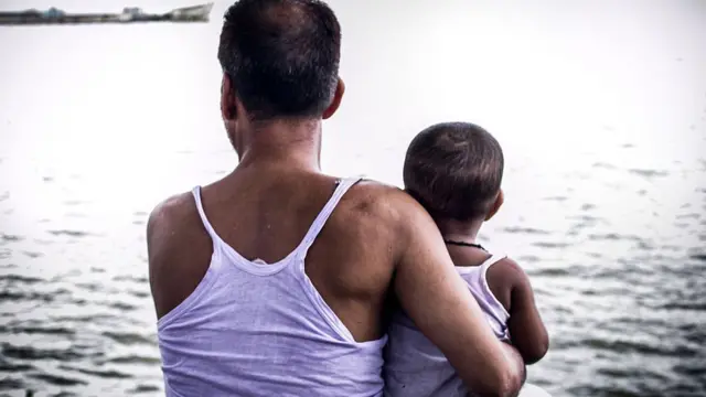 সন্তানকে নিয়ে নদীর পাড়ে বসে আসেন এক বাবা।