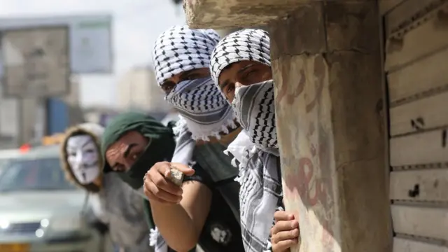 Jóvenes palestinos con el rostro cubierto, se esconden detrás de una pared
