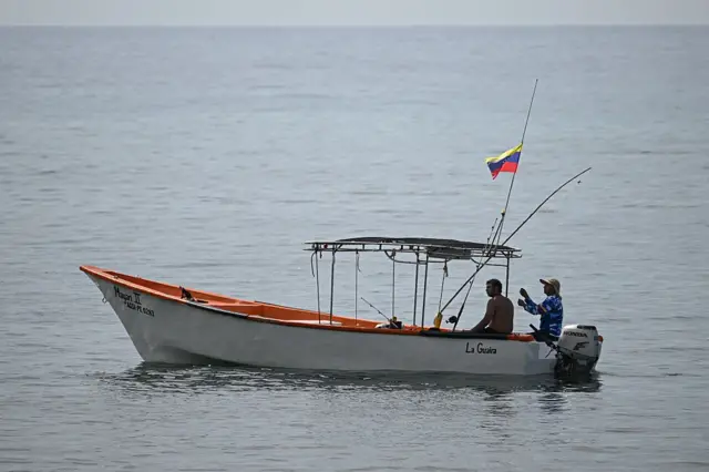 Dos pescadores navegan en un bote con la bandera de Venezuela.
