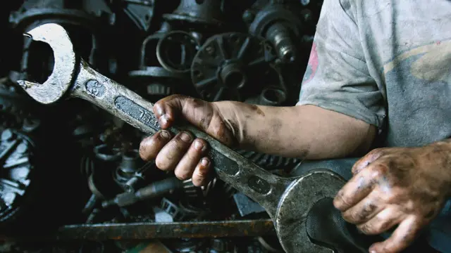 Sanayide çalışan bir çocuğun motor yağından kararmış elleri, kıyafetleri ve bazı motor parçaları görülüyor.