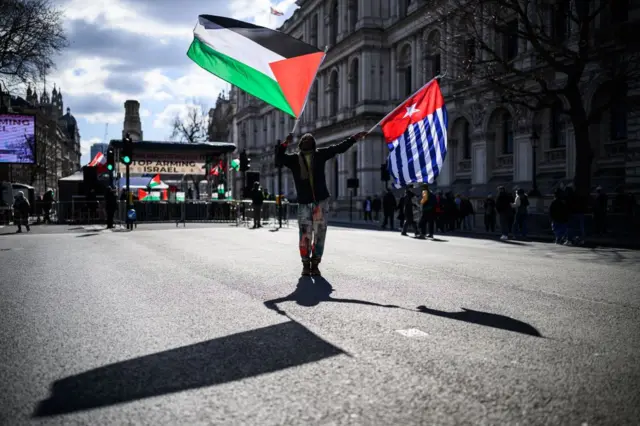 Seorang pria mengibarkan bendera Palestina (kiri) dan Bintang Kejora (kanan) menjelang unjuk rasa di akhir Pawai Nasional untuk Palestina, pada 15 Maret 2025 di London.