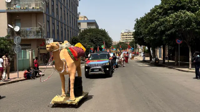 ምስሊ ናይታ ሃገራዊ ኣርማ ኤርትራ ዝኾነት ገመል እትመርሖ ካርኒቨላ ኣስመራ ብጐደናታት እናሓለፈ። ባንዴራ ኤርትራ ዝተሸለመት ሚከናን ተሳተፍቲን ደድሕሪኣ እናሰዓቡ
