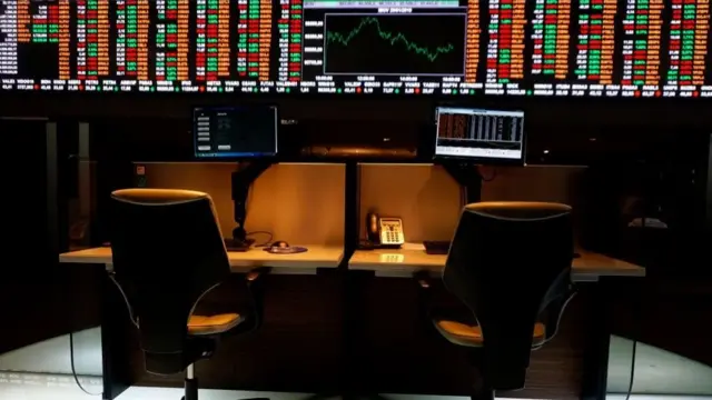 Escritorio con pantalla de cotización de bolsa detrás.
