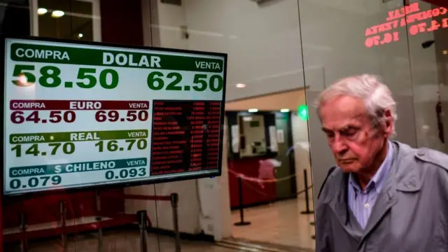 Hombre camina por la calle en Buenos Aires bajo un cartel con el valor de compra y de venta del dólar el 28 de octubre de 2019.