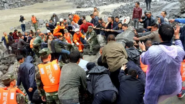 Rescue workers and local residents pull on a rope to move a large boulder at the site of a landslide in Xinmo village, Maoxian county, Sichuan province, China, 24 June 2017